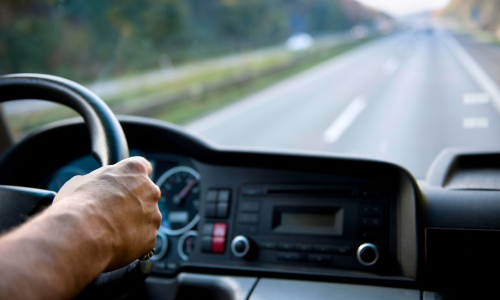 Hands on a steering wheel of a vehicle driving on the road.
